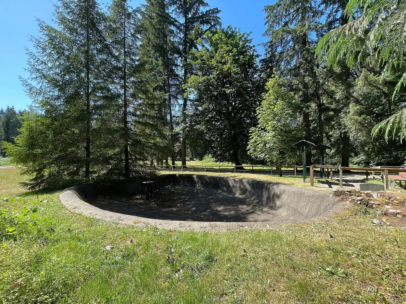Empty concrete basin at the Flaming Geyser site on a sunny lawn ringed by tall evergreens