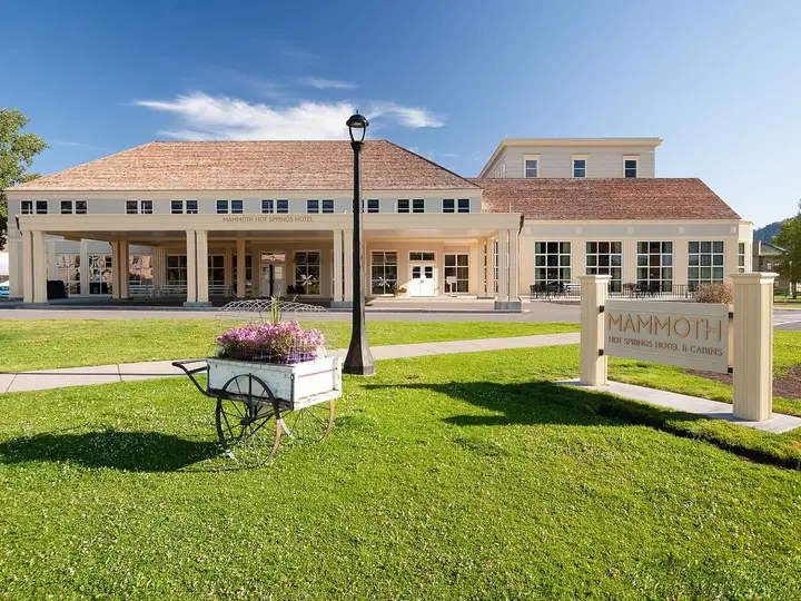 Mammoth Hot Springs Hotel exterior with covered entrance, lawn and Mammoth sign under blue sky