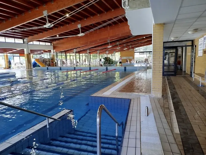 Indoor swimming pool with steps and wooden ceiling beams at Várkertfürdő in Pápa