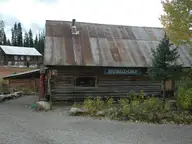 Rustic log lodge with a Burgdorf sign and rusted metal roof beside a gravel lot at Burgdorf Hot Springs
