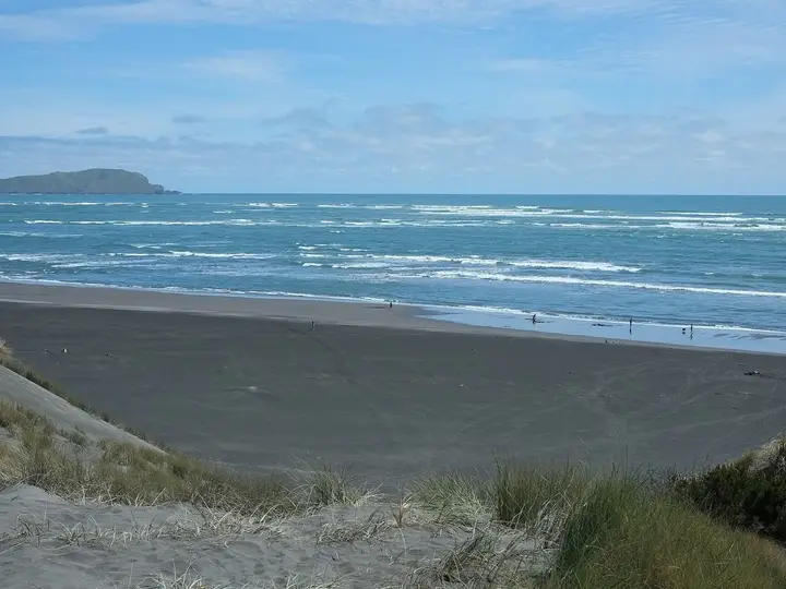 Black sand Ocean Beach near Kawhia seen from the dunes, with surf and a distant headland