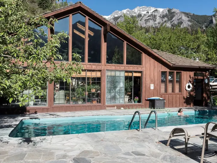Outdoor mineral pool beside the timber and glass lodge at Wiesbaden Hot Springs under mountain peaks in Ouray