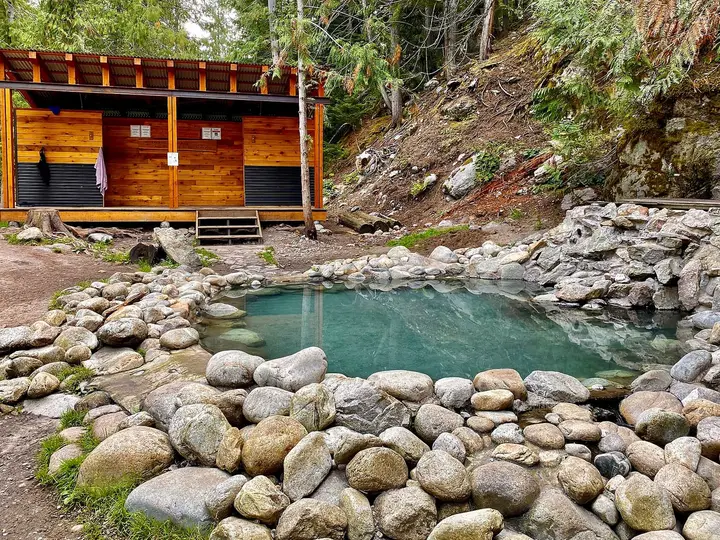 Rock-lined main pool at Halfway River Hot Springs beside a wooden change shelter in the forest