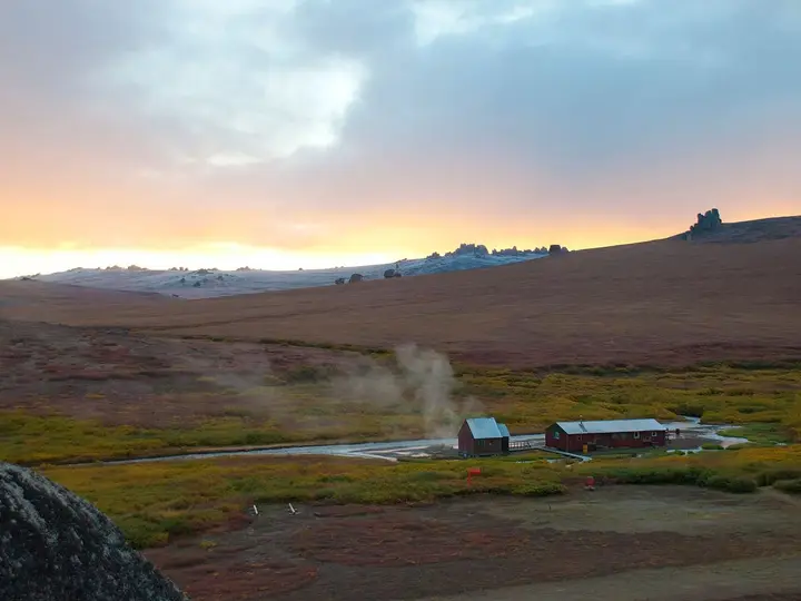 Steam rising beside the bathhouse and bunkhouse at Serpentine Hot Springs under a sunrise sky