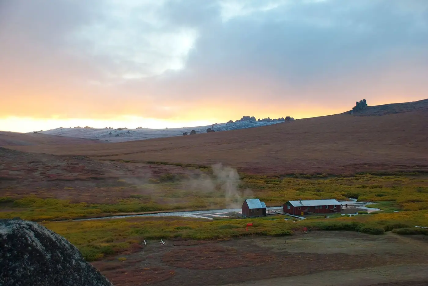 Steam rising beside the bathhouse and bunkhouse at Serpentine Hot Springs under a sunrise sky