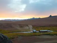 Steam rising beside the bathhouse and bunkhouse at Serpentine Hot Springs under a sunrise sky