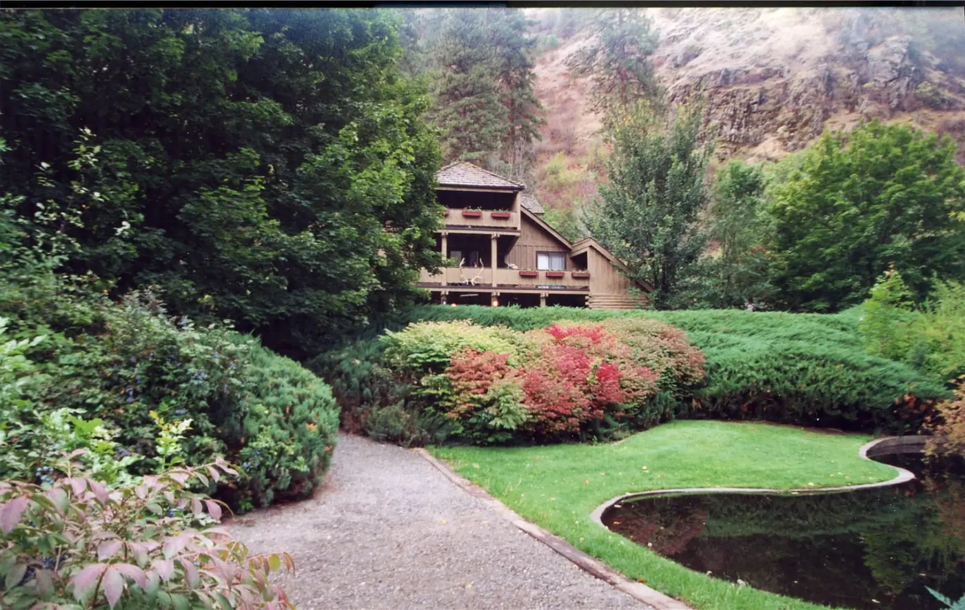 Wooden lodge at the former Riggins Hot Springs guest property behind gardens, lawn and a curved pond