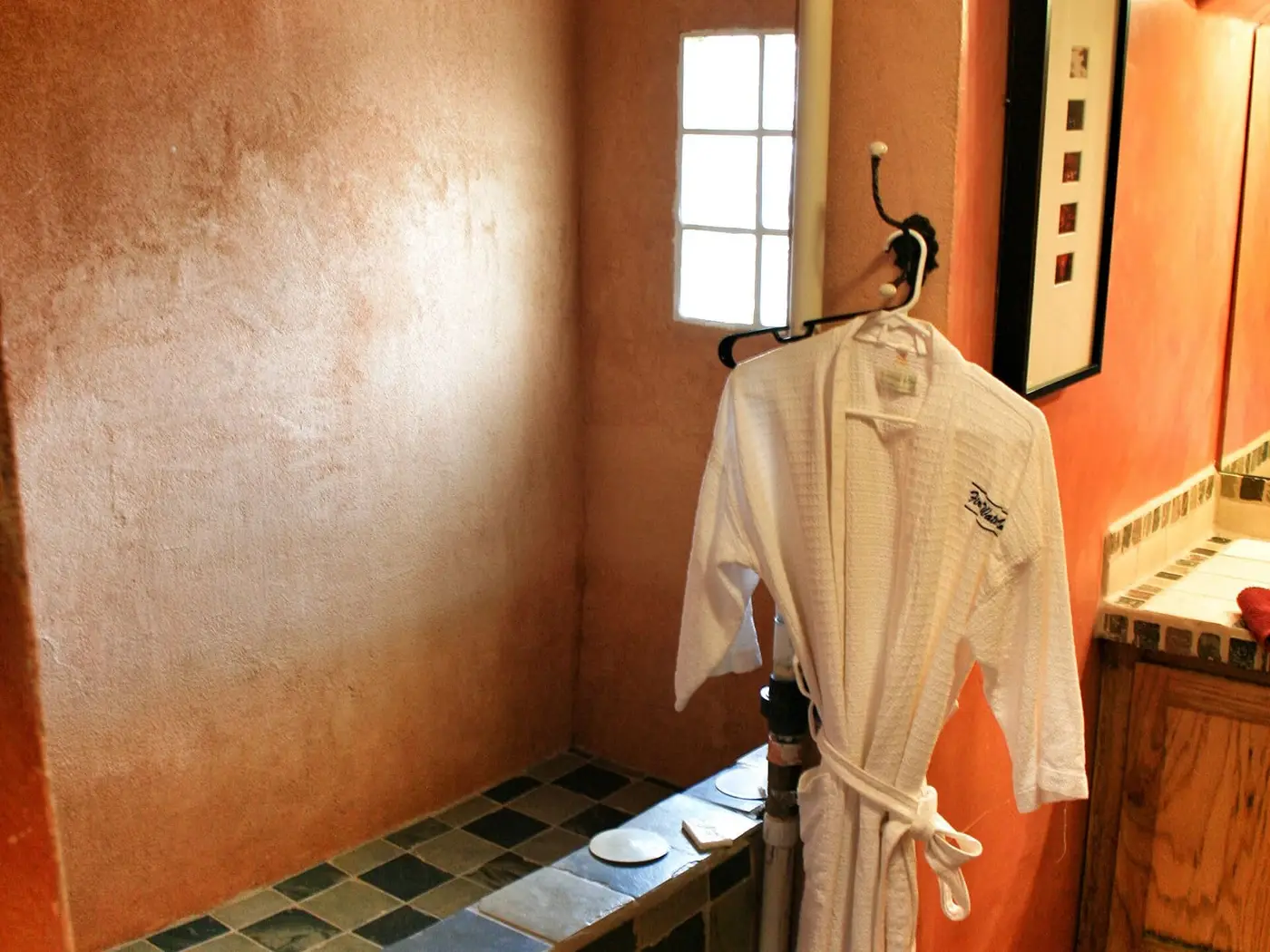 Terracotta walled bath room at Fire Water Lodge with a tiled soaking area and a white robe