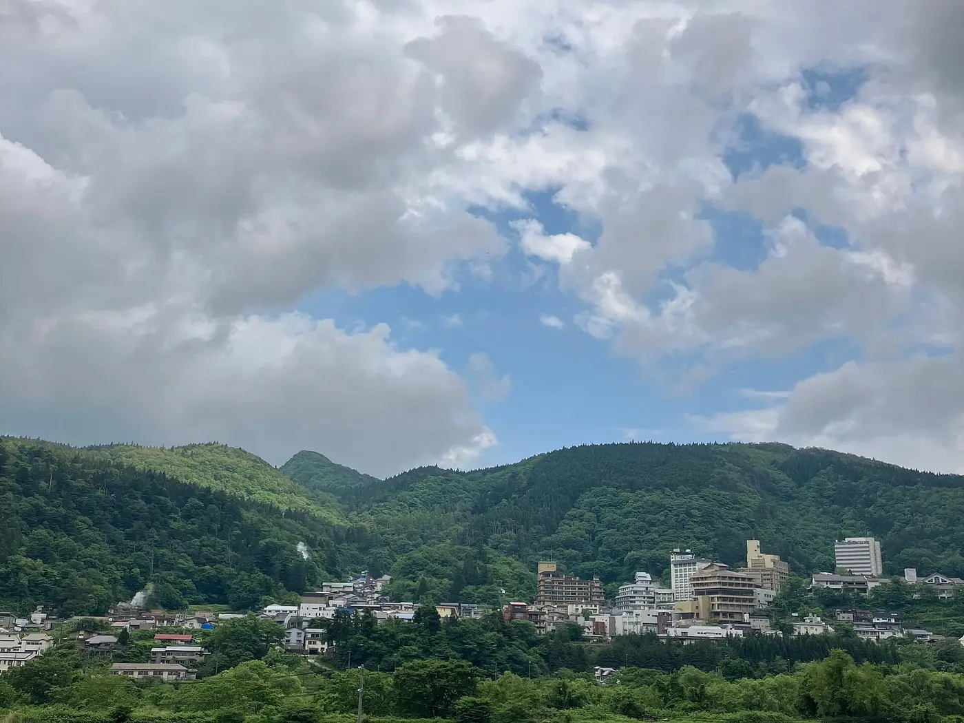 Distant view of Naruko Onsen town in a green mountain valley under clouds