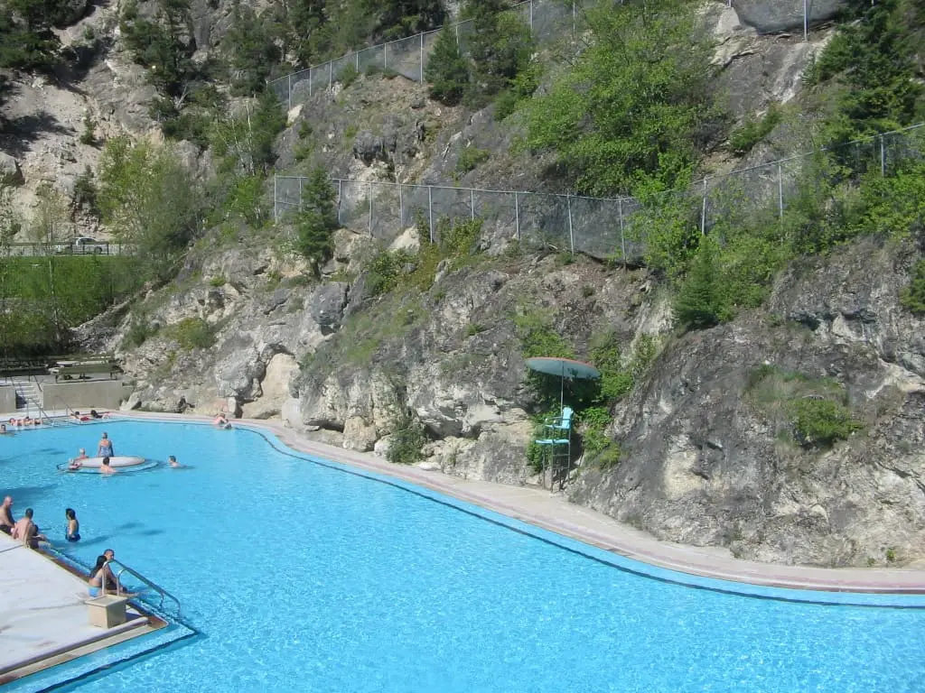 Large blue hot pool at Radium Hot Springs below steep rocky cliffs