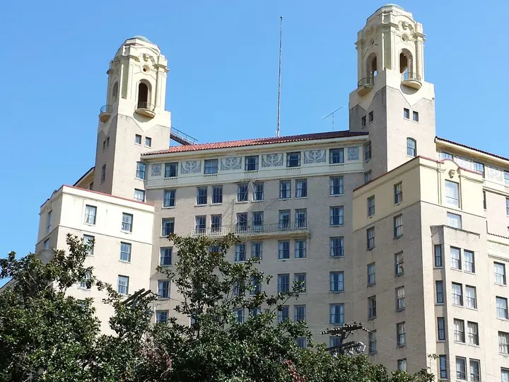 Twin towers of the historic Arlington Hotel rising above trees and a green lawn in Hot Springs