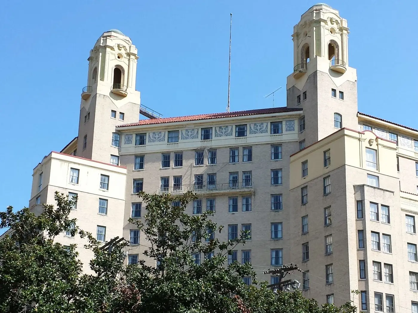 Twin towers of the historic Arlington Hotel rising above trees and a green lawn in Hot Springs