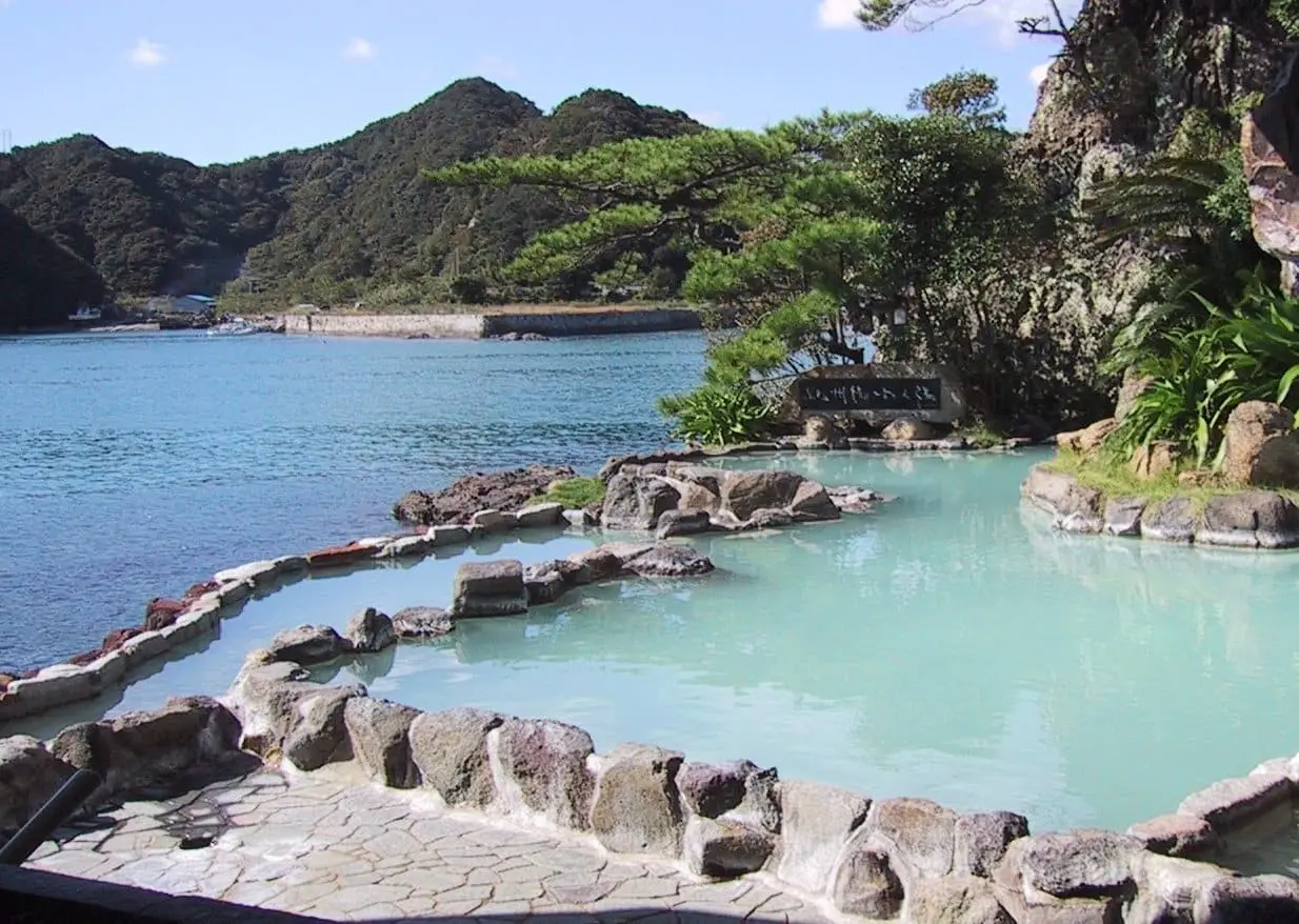 Milky blue outdoor onsen pool with rock edges overlooking the bay at Nakanoshima, Nachikatsuura