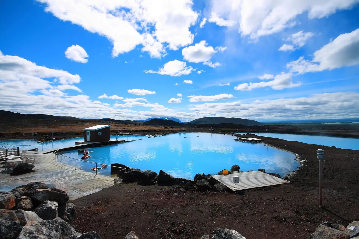 Milky blue geothermal lagoon at Mývatn with wooden decks and lava rocks under a bright sky