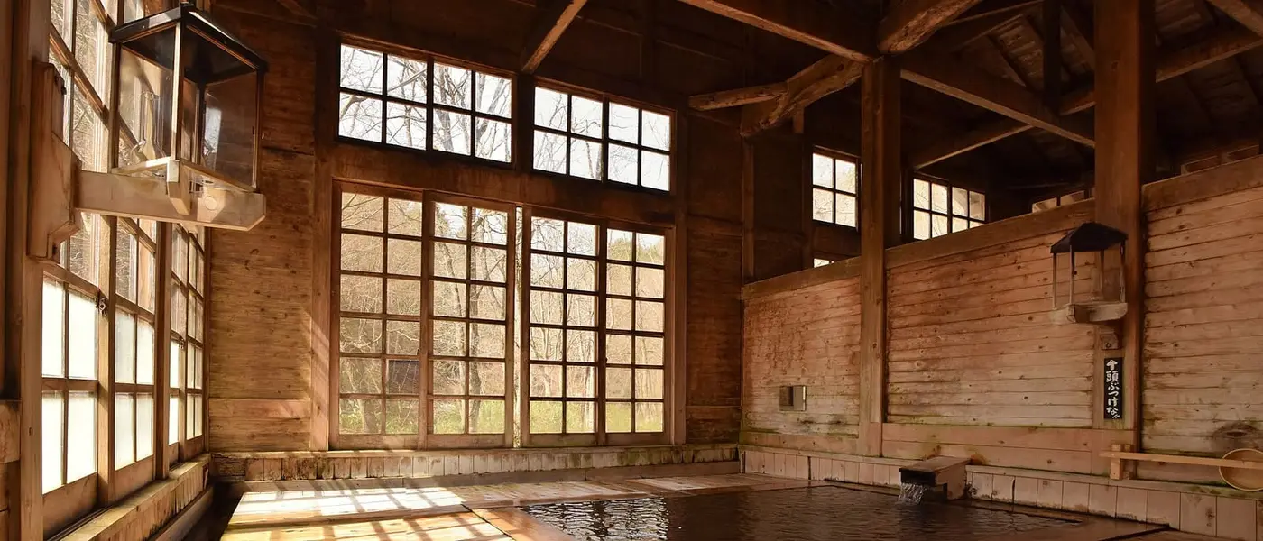 Wooden bath hall at Aoni Onsen with large paned windows and a shallow indoor bath