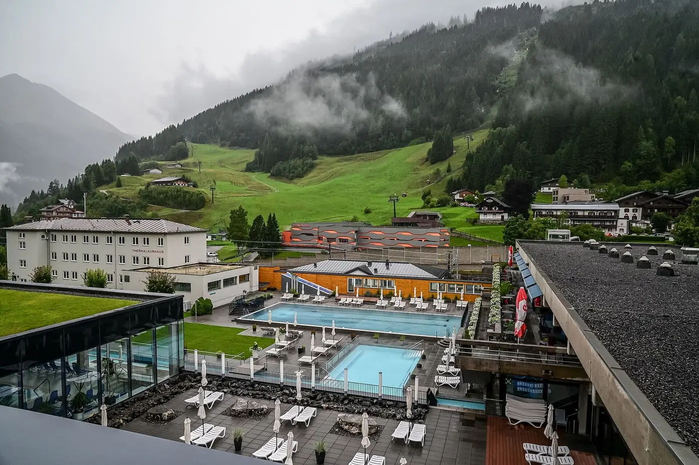 Outdoor thermal pools of the Felsentherme Bad Gastein below misty green mountain slopes