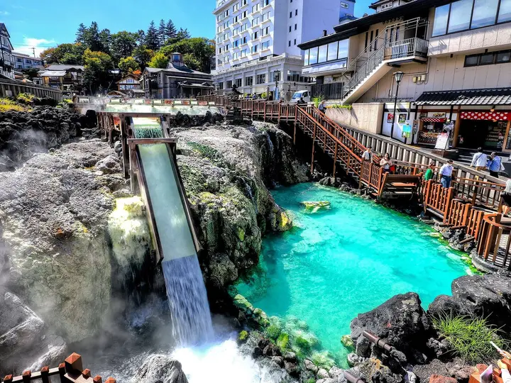 Turquoise hot water of the Kusatsu Onsen Yubatake pouring down a steaming channel beside wooden walkways
