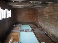 Wooden bath hut interior with pale blue sulfur water in a long tub at Osorezan Onsen