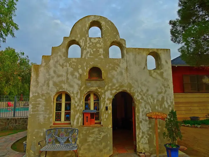 Arched stucco registration office at Mercey Hot Springs, with the fenced pool visible at left