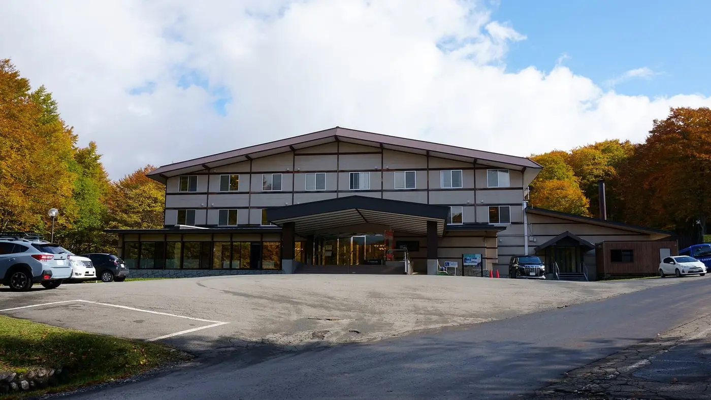Kyukamura Nyuto Onsenkyo lodge building and parking area surrounded by autumn trees under a blue sky