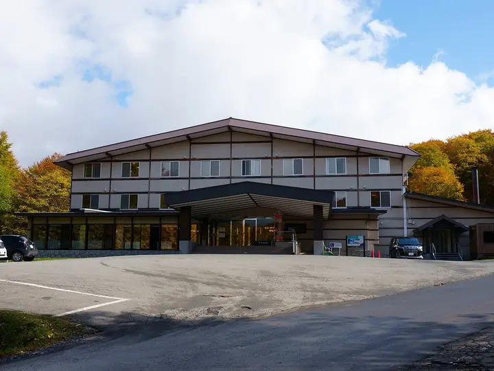 Kyukamura Nyuto Onsenkyo lodge building and parking area surrounded by autumn trees under a blue sky