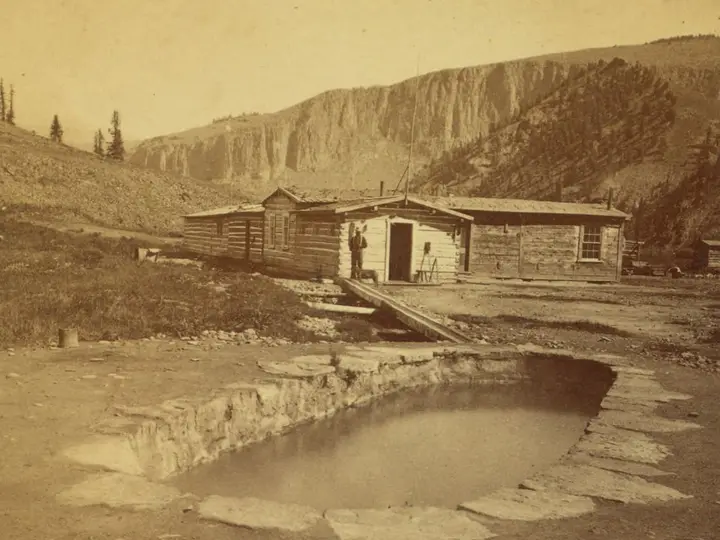 Historic photograph of the stone rimmed Hot Sulphur Spring pool and cabins at Wagon Wheel Gap below cliffs