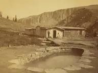 Historic photograph of the stone rimmed Hot Sulphur Spring pool and cabins at Wagon Wheel Gap below cliffs