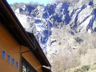 Timber clad Terme di Premia building below a tall waterfall on granite cliffs in Valle Antigorio
