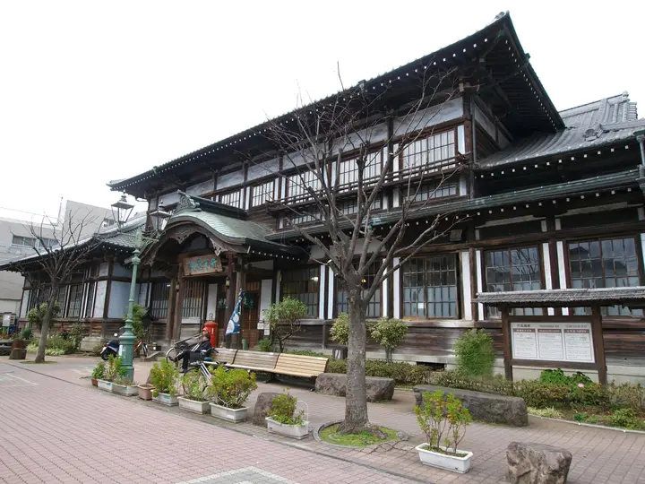 Historic wooden Takegawara Onsen bathhouse with tiled roofs and a tree lined forecourt in Beppu